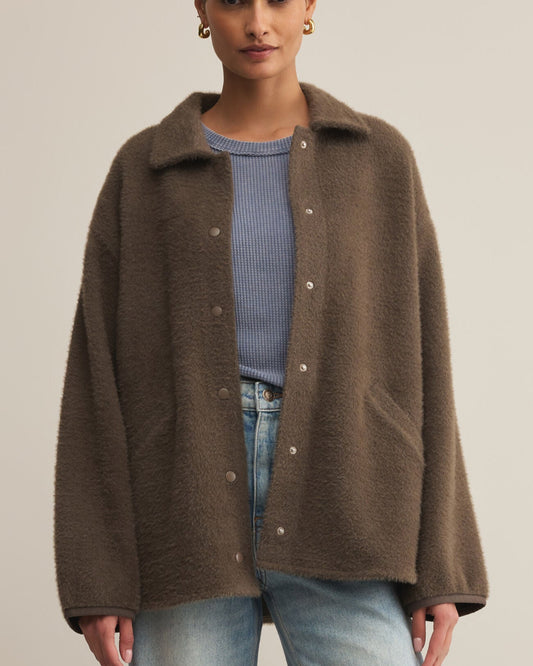 Woman wearing a brown coat over a blue sweater and jeans on a beige background