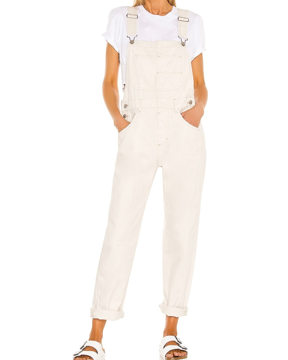 Model wearing Free People Ziggy Denim Overalls in Parchment color wearing Sandals on a white background