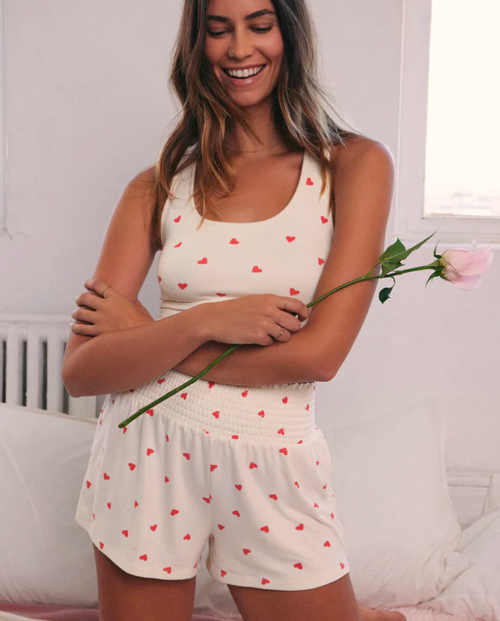 Model wearing Z Supply Dawn Heart Shorts with matching tank top holding a rose on a white background