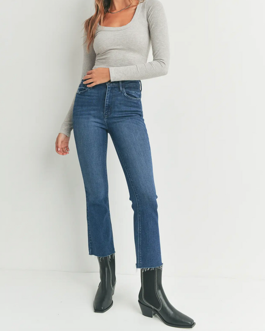 Model wearing Just Black Denim High Rise Tonal Crop Flare dark wash wearing black boots and a gray shirt on a white background