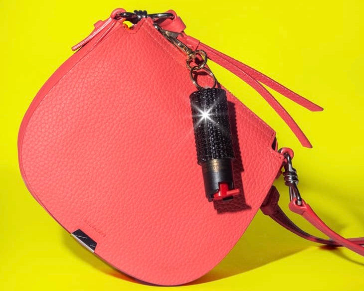 Image of a Pink Purse with black blingsting pepper spray attached to it on a neon yellow background