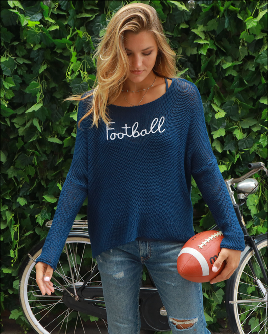 Model wearing Wooden Ships Middlebury Blue Football Stitched Crew wearing jeans and holding a football in front of green vines 