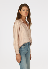 Model wearing Dylan Subtle Shimmer Siena Shirt in pink wearing jeans on a white background