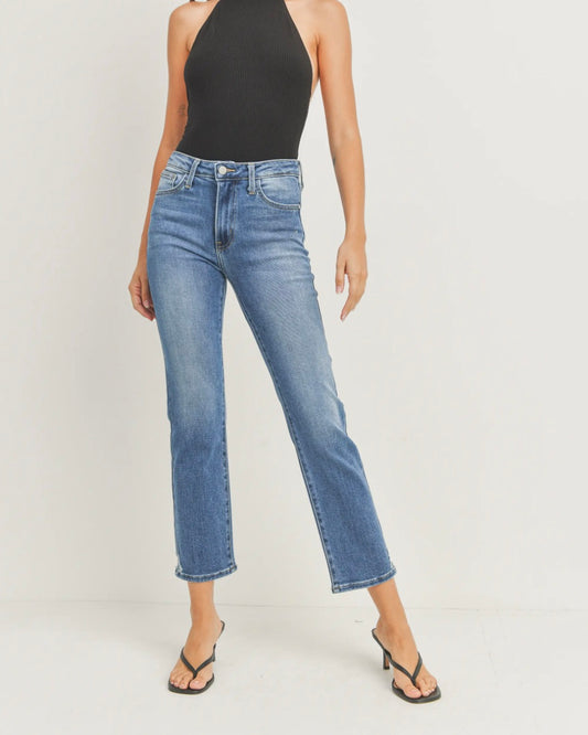 Model wearing Just black denim slim straight jeans in a medium wash mid rise wearing black open toed shoes and a black tank top on a white background