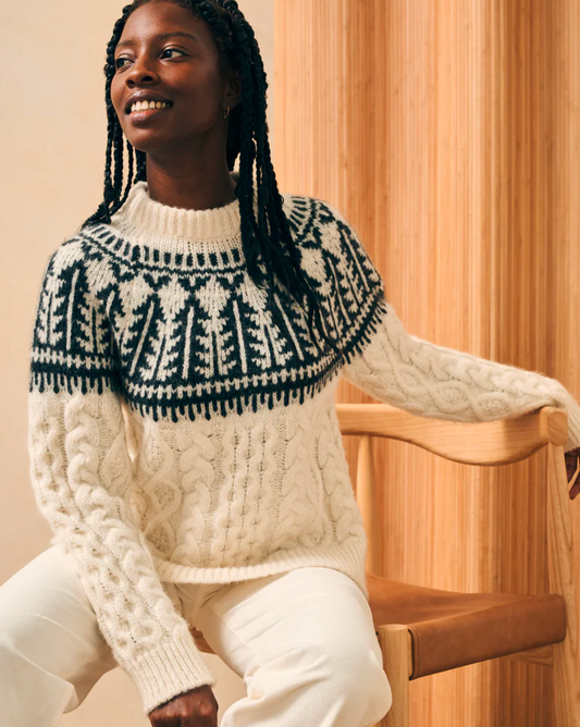 Model wearing Faherty Native Knitter Frost Fairisle in white sheep cam wearing white pants sitting on a chair