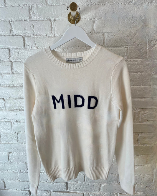Middlebury College MIDD white sweater with blue letters from Ellsworth+Ivey on a white brick wall background