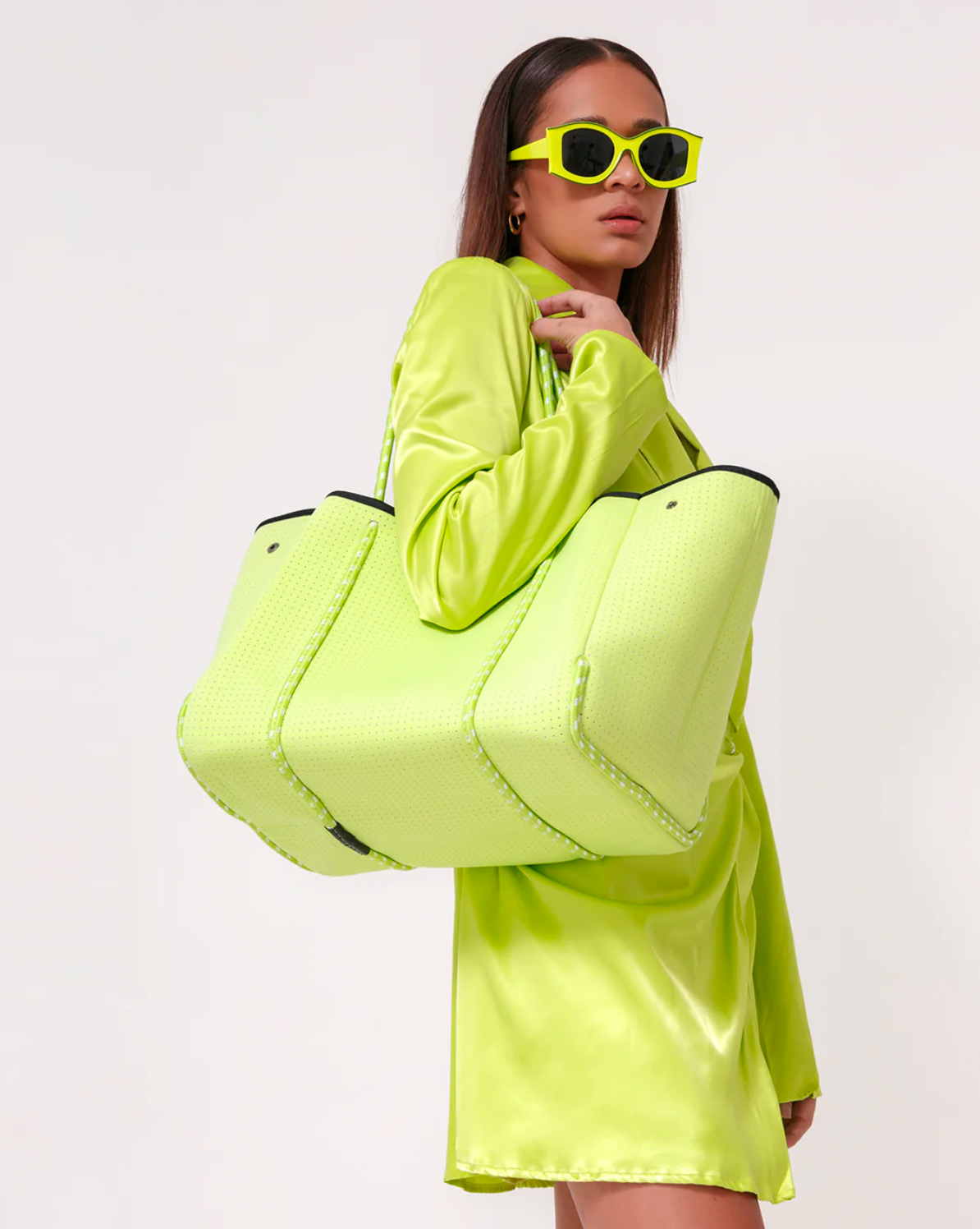Model wearing POPUPS neon green everyday neoprene tote wearing neon green dress and glasses on a white background