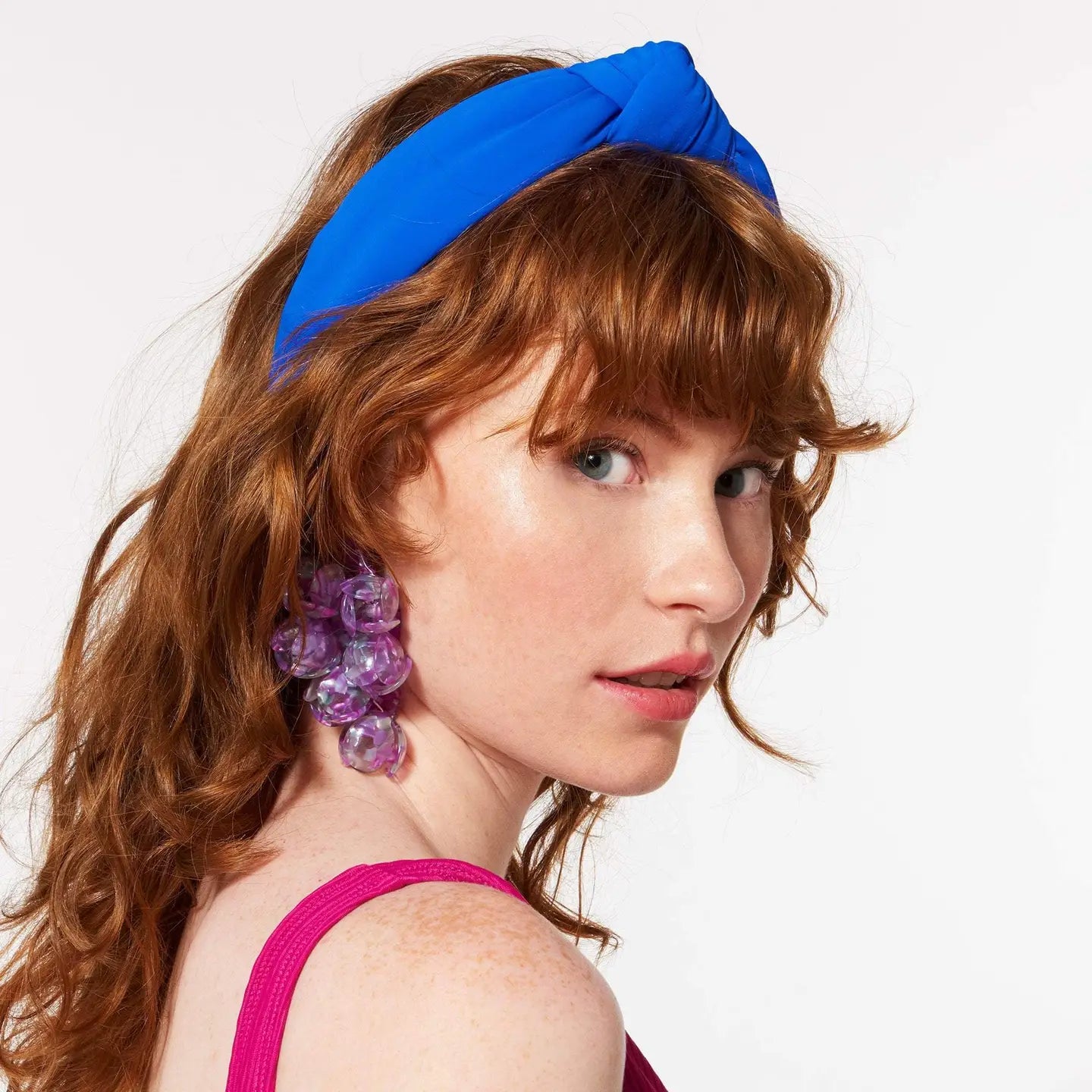 Model wearing Lele Sadoughi Royal Blue Neoprene headband wearing purple earrings and pink top on a white background