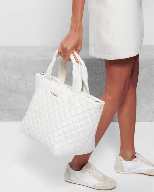 Model holding MZ Wallace Pearl Metallic Medium Metro Tote Deluxe bag wearing white shoes and a white skirt on a white background