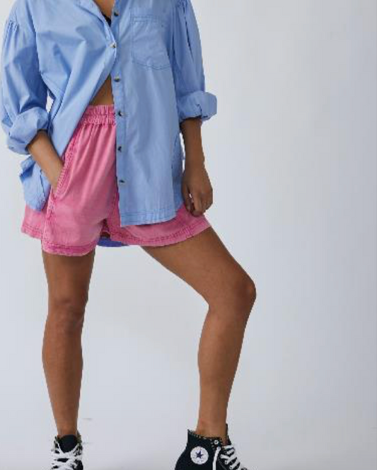 Model wearing Free People get free chambray pull on shorts in Gumdrop color wearing a blue shirt and black converse shoes on a white background 