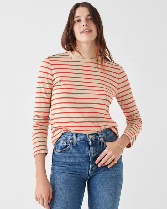 Model wearing Faherty long sleeve Tee in orange spicy stripe wearing jeans on a white background