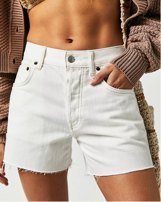 Model wearing Free People Ivy Mid Rise Shorts in crystal clear white showing belly and wearing brown sweater crop on a white background