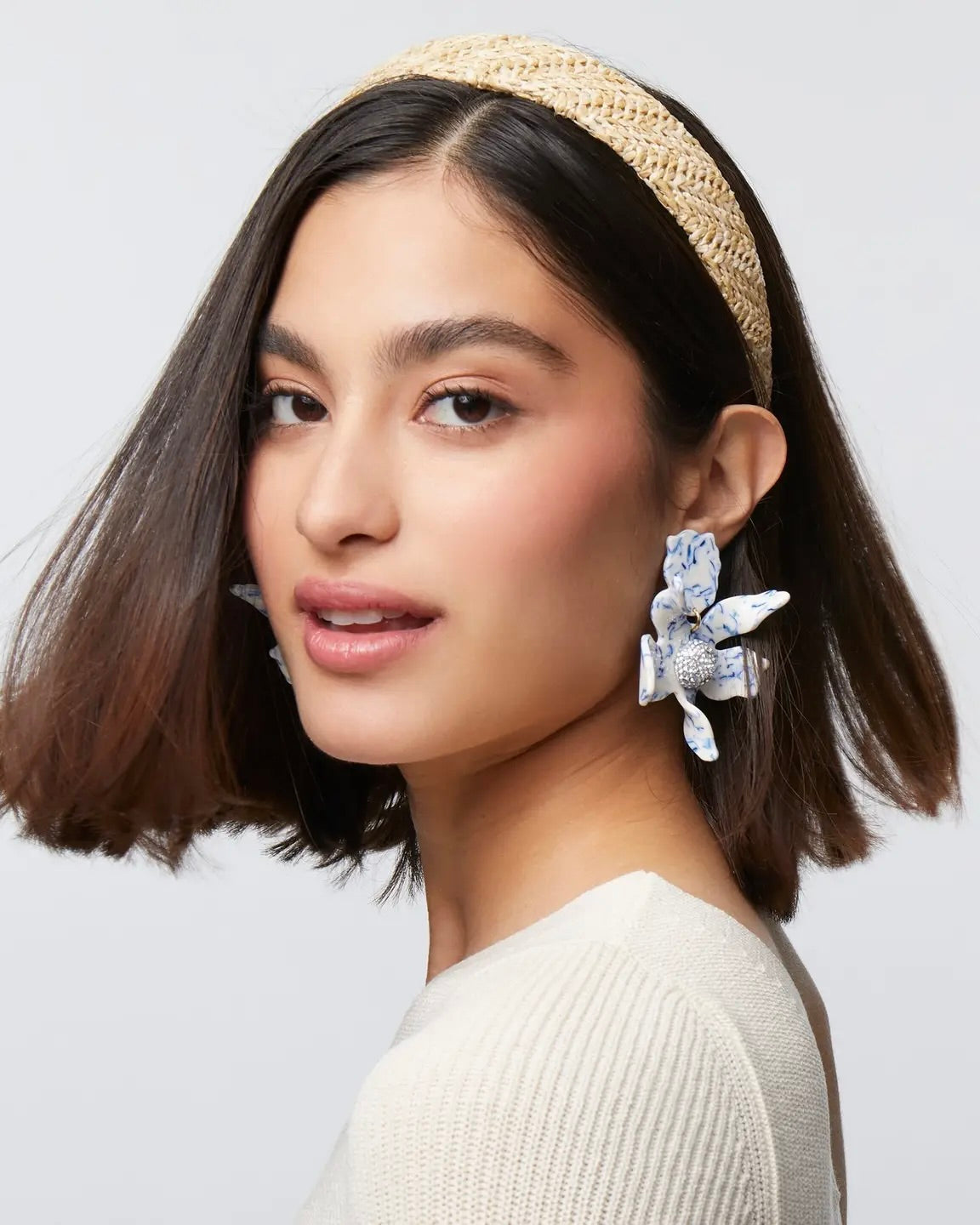 Model wearing Lele Sadoughi Natural Raffia Bessette Headband wearing Big earrings and a white top on a white background