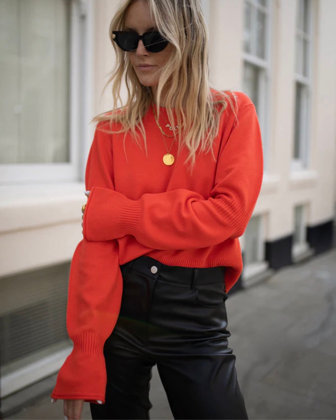 Model wearing French Connection Babysoft Crewneck Gather Jumper sweater in Fiery Red wearing black faux leather pants and sunglasses in a building 