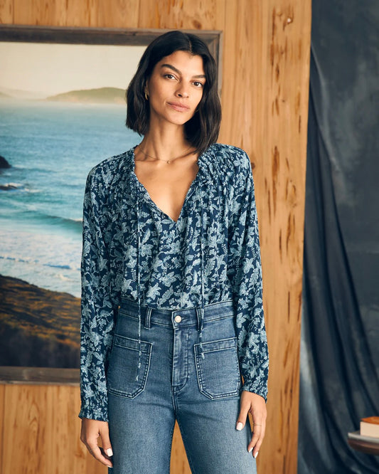 Model wearing Faherty Emery Blouse wearing Jeans standing in front of wooden wall and ocean painting