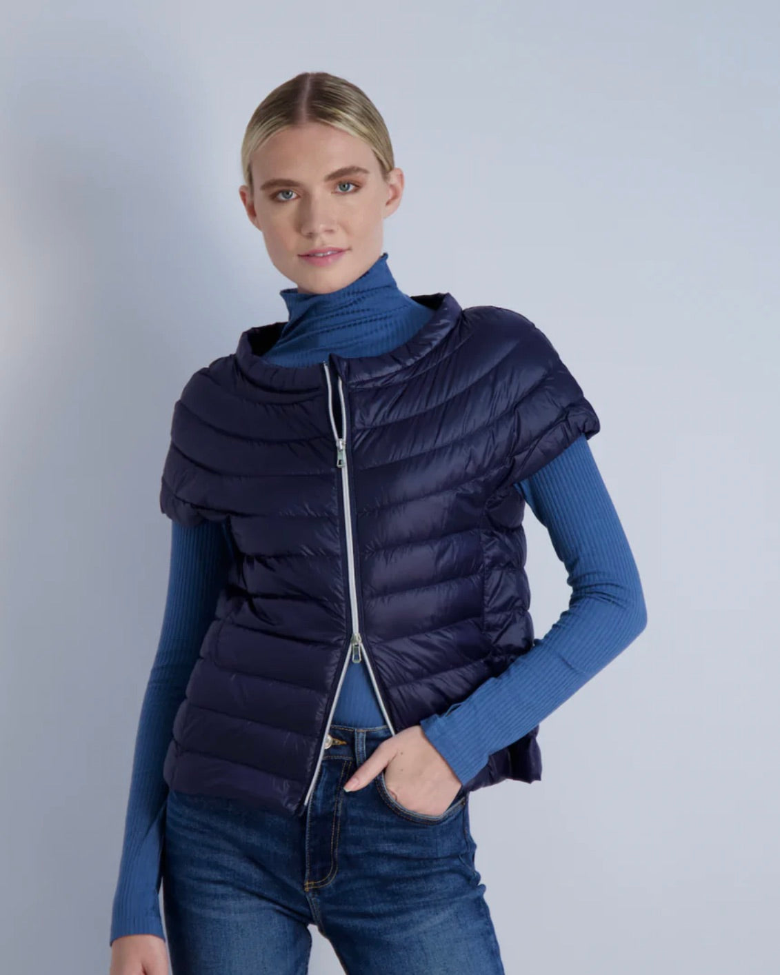 Model wearing Cotes of London Ink Navy St Ives Down Vest wearing jeans and a blue turtleneck on a light blue background