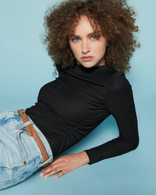 Model wearing Nation Mock Neck Long sleeve shirt in black wearing jeans on a blue background